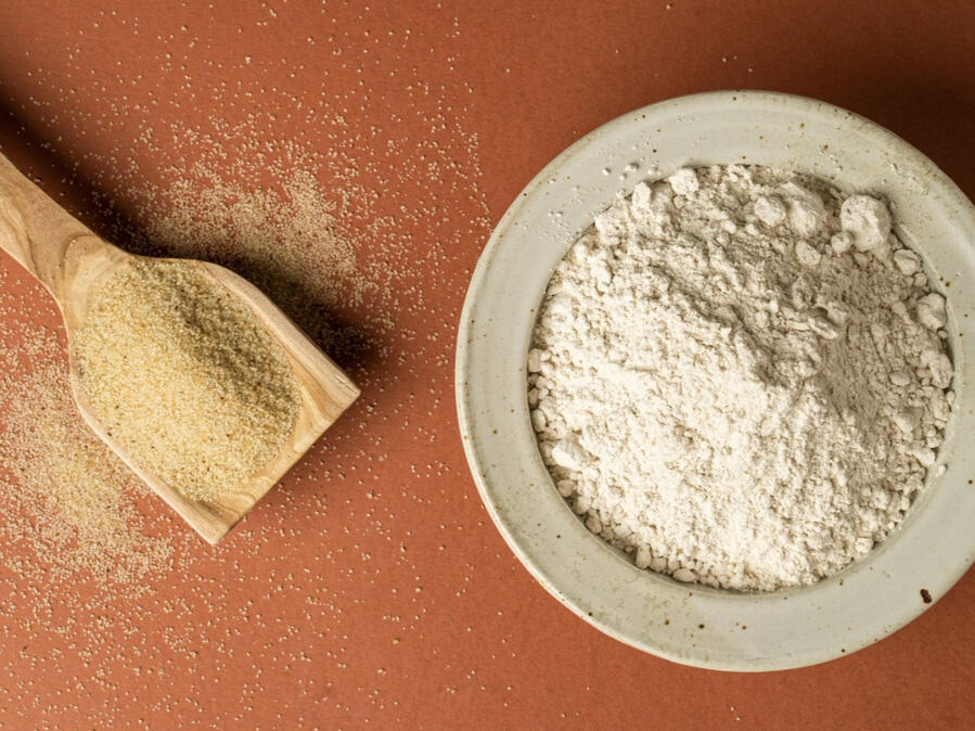 Fonio grain on a wooden scoop beside a bowl of fonio flour